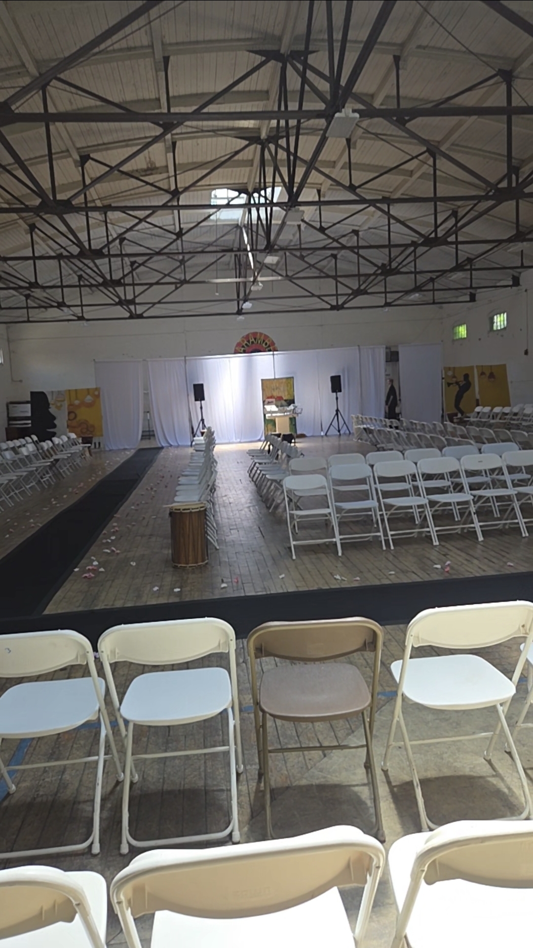 Community event hall set with white chairs, draped stage, and DJ speakers ready before the program begins