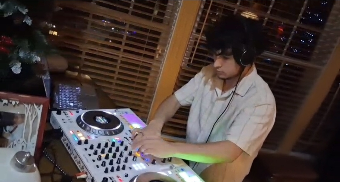 DJ Aiden Jules mixing on a white controller at a private home celebration with festive lighting and holiday decor
