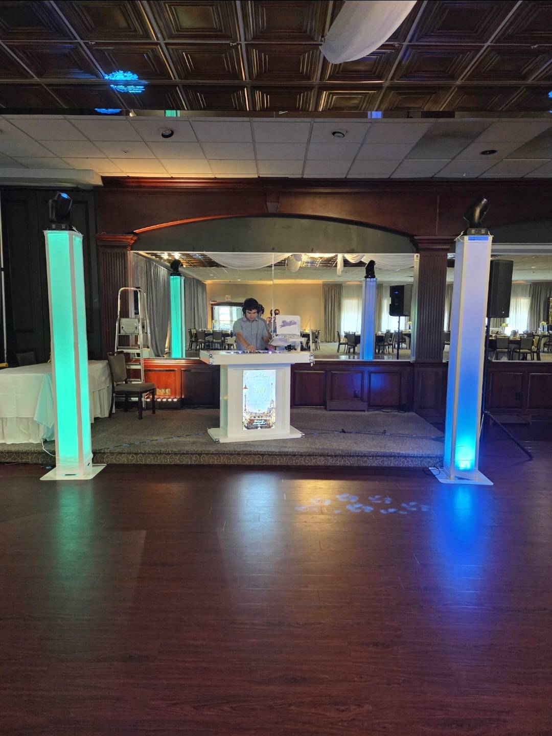 Professional DJ setup on a ballroom stage with illuminated columns and a white booth