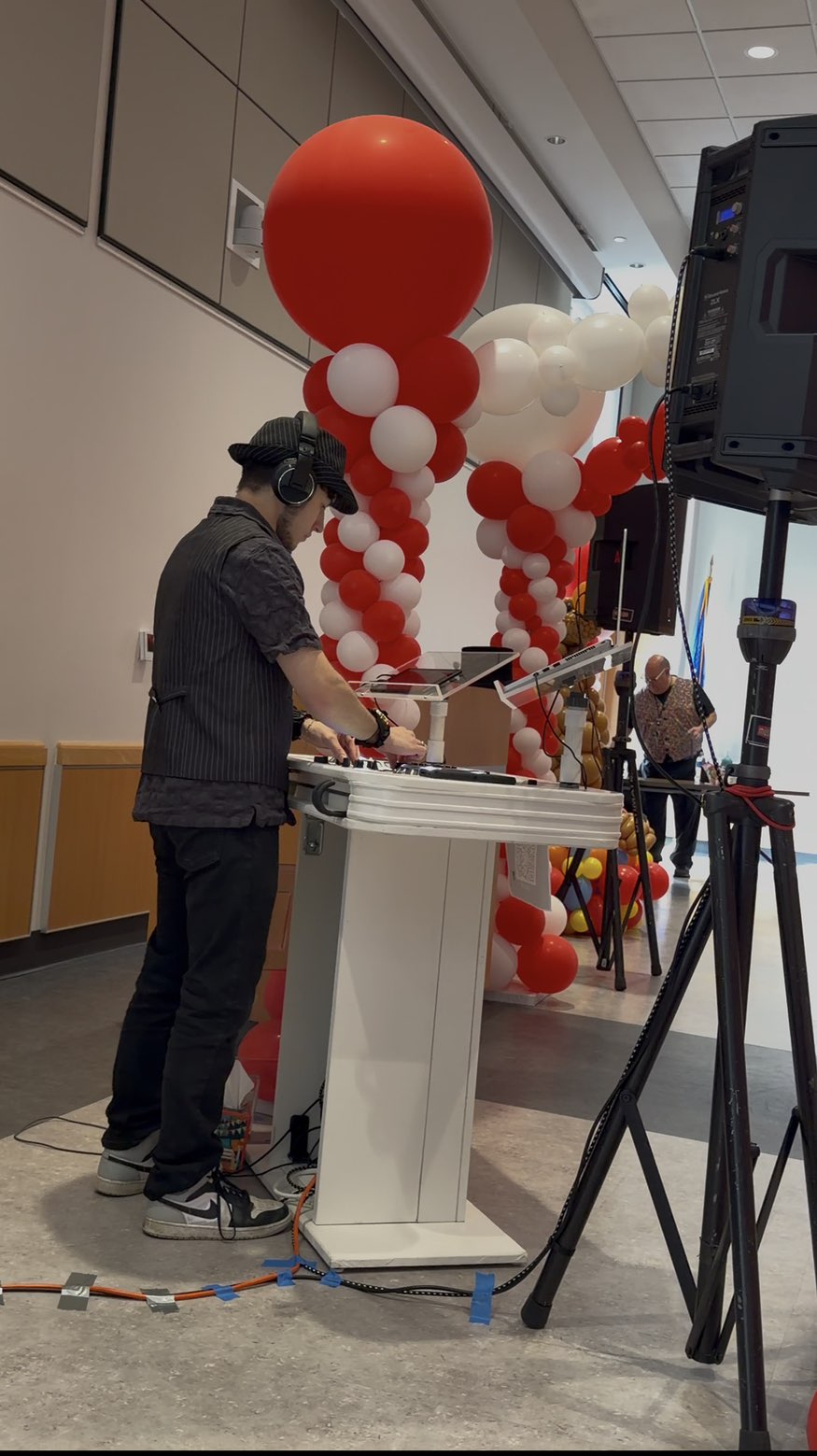 DJ Aiden Jules performing at a college event beside red and white balloon columns with professional speakers on stands