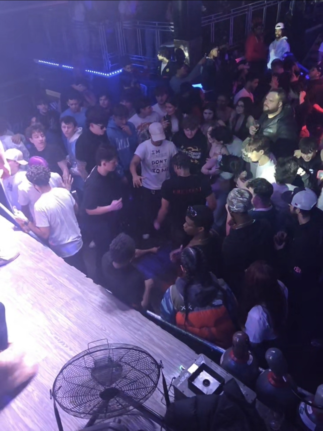Packed nightclub dance floor viewed from above with LED strips, blue wash lighting, and dense crowd energy