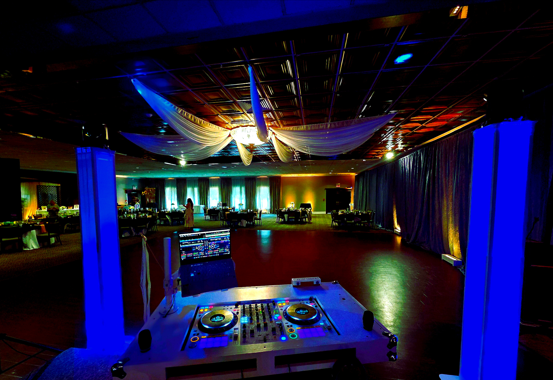 Elegant wedding reception ballroom with draped ceiling, uplighting, and DJ Aiden Jules' booth ready for the celebration