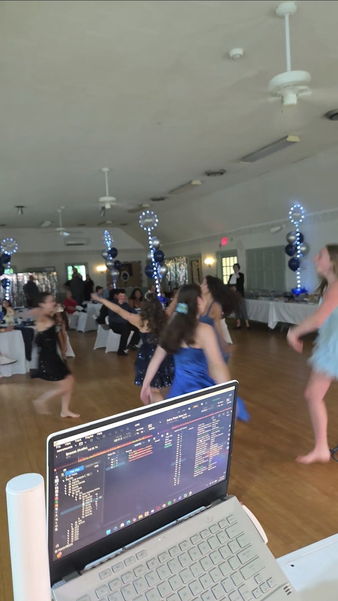 Guests dancing at a Sweet 16 with balloon columns and DJ laptop in foreground