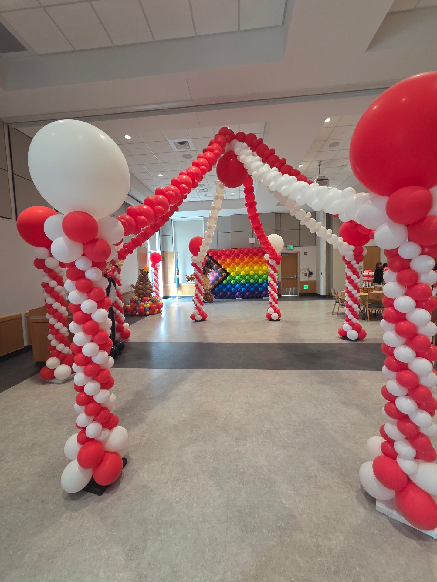Red and white balloon arch entryway leading into a college event space with a rainbow balloon wall in the background
