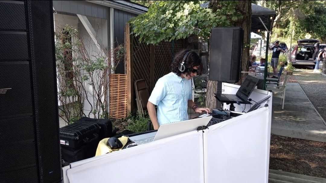 DJ Aiden Jules mixing at a white event booth with Bose speakers at an outdoor community gathering
