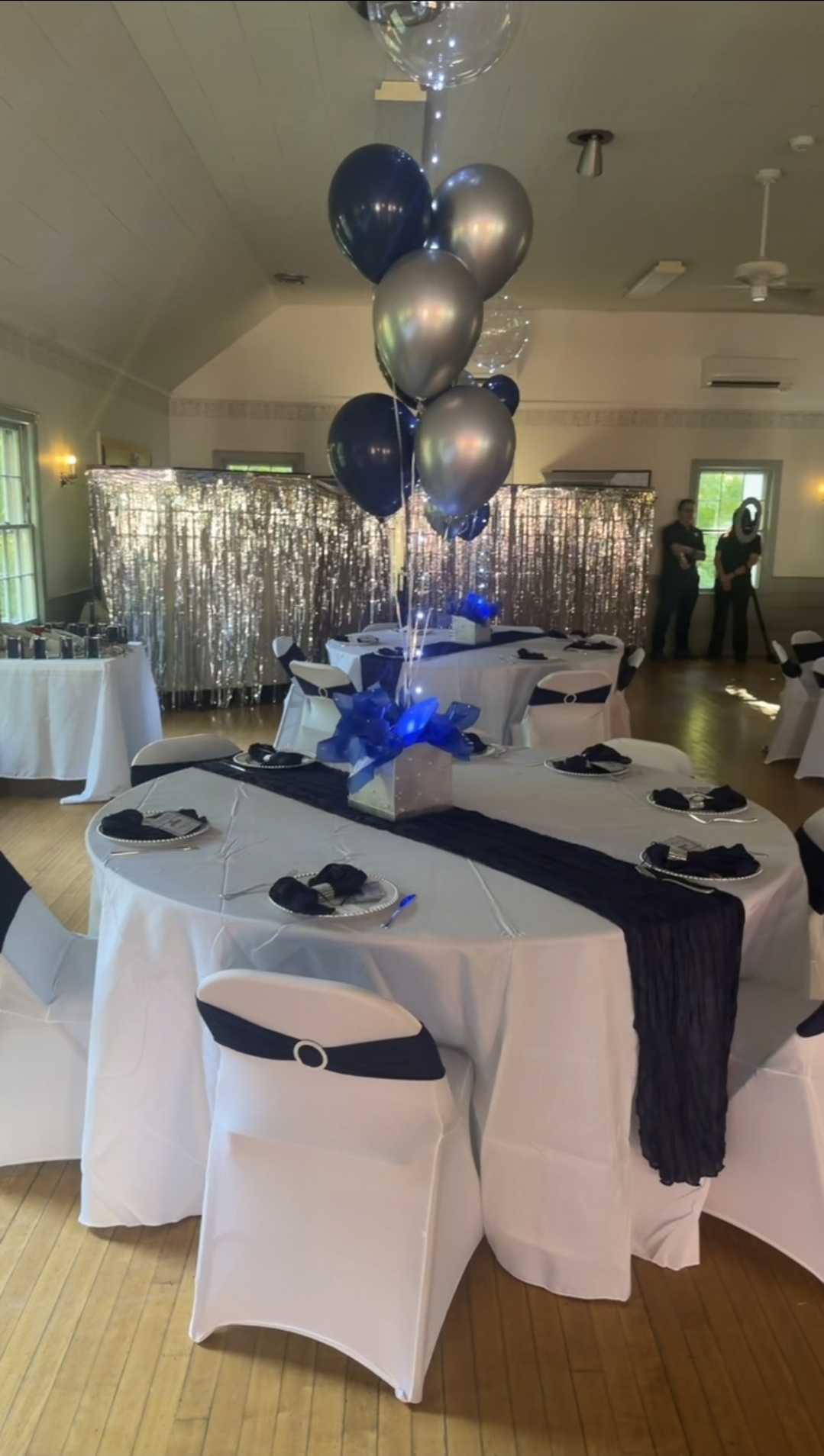Elegant Sweet 16 reception tables with navy runners, silver backdrop, and navy and silver balloon centerpieces