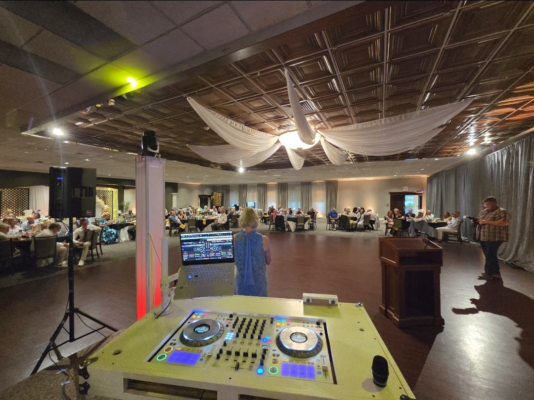Anniversary reception ballroom with draped ceiling, uplighting, and DJ controller in foreground