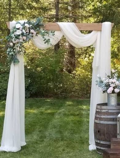 Outdoor wedding ceremony arch draped in white fabric and florals