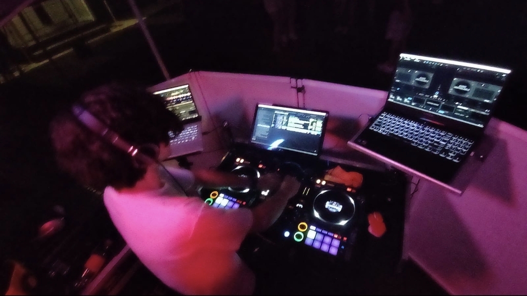 DJ Aiden Jules mixing on a Pioneer controller at an outdoor birthday party with pink and purple stage lighting