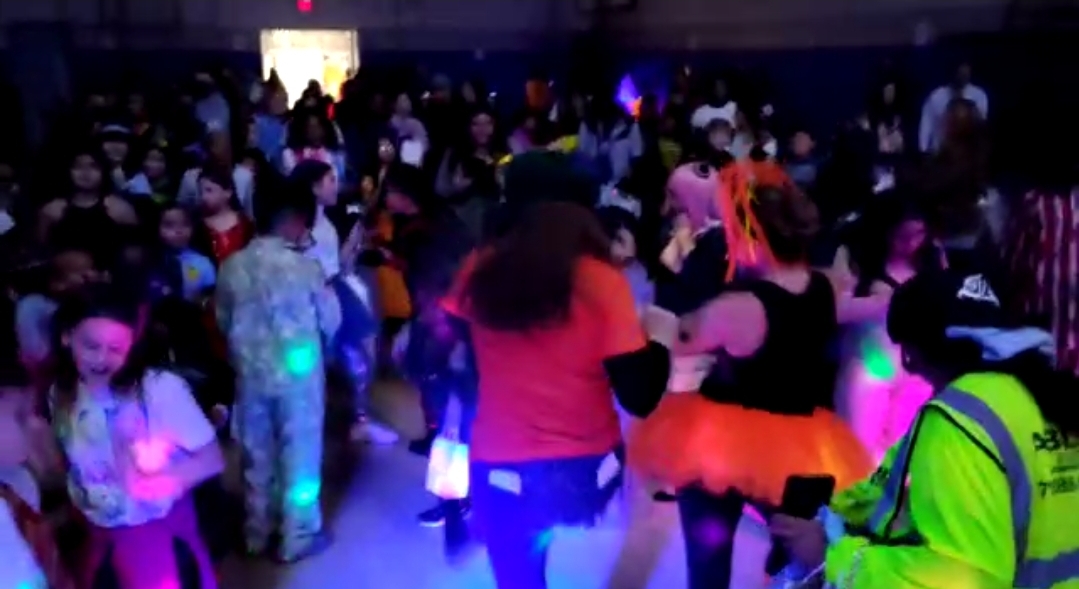 Costumed students dancing under colored lights at a school Halloween dance