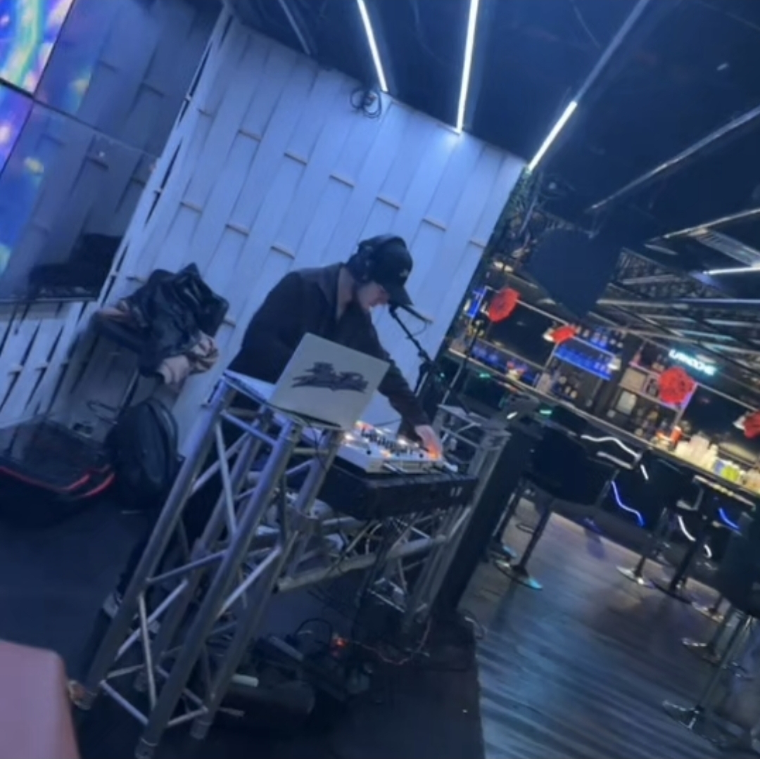 DJ Aiden Jules performing on an elevated white truss booth with linear LED accents inside a club
