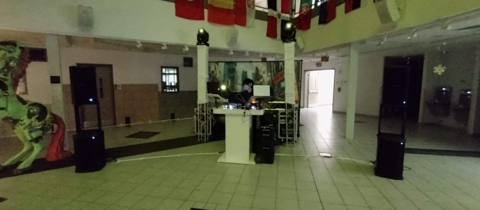 DJ Aiden Jules booth set up in a school venue with truss lighting, moving heads, and flags overhead